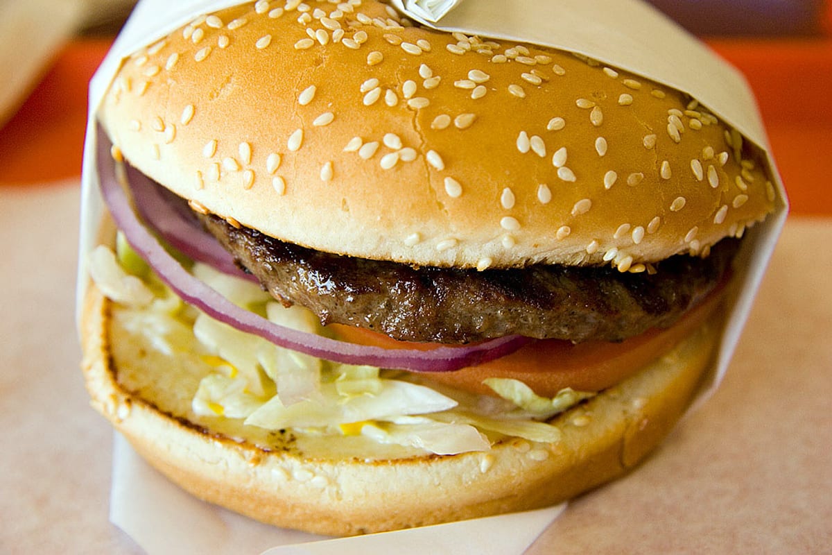 A plain fast-food hamburger with lettuce, tomato, and onion on a sesame bun